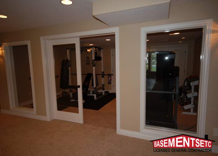 Interior view of a basement gym with exercise equipment and glass doors.