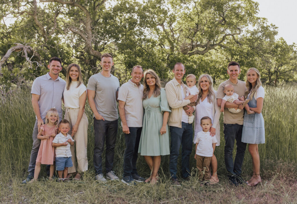 A family portrait in a grassy area, featuring adults and children smiling together.