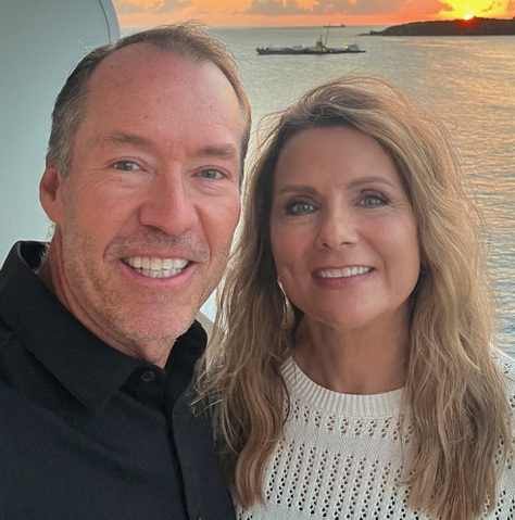 Two people smiling together with a sunset over water in the background.