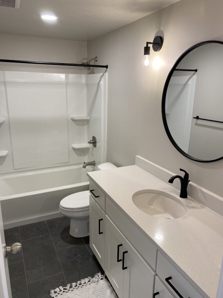 Modern bathroom with a shower, white vanity, and round mirror.