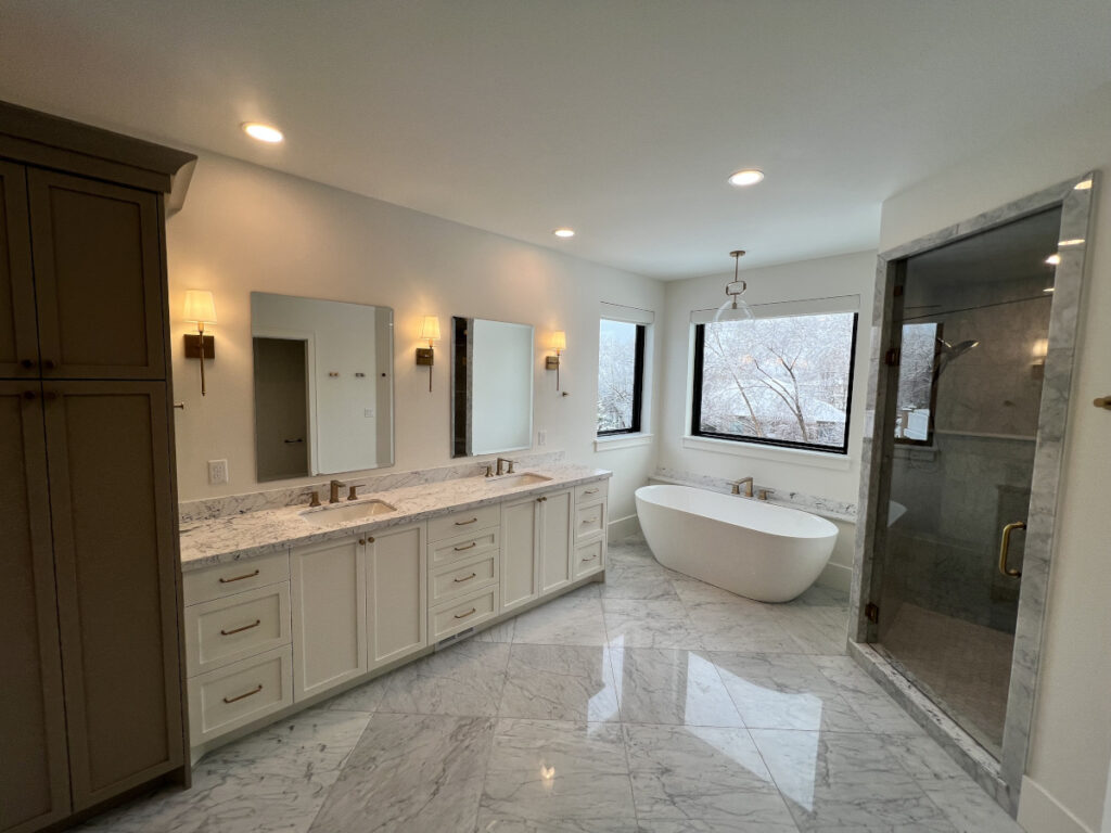 Modern bathroom with double vanity, freestanding tub, and large windows.