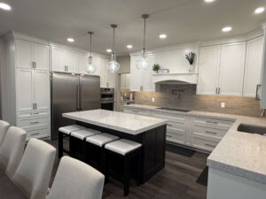 Modern white kitchen remodel with quartz island, custom cabinetry, stainless steel appliances, and pendant lighting.